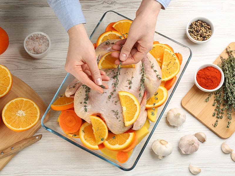 Woman Adding Thyme Raw Chicken